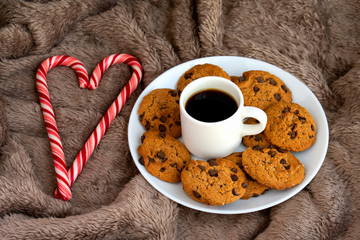 Delicious homemade chocolate cookies, caramel canes,  cup of coffee on soft blanket. Christmas spirit.