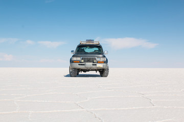 Fototapeta na wymiar Car on the Uyuni Salar in Bolivia. Blue Sky and white salt background.