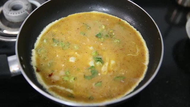 cooking omlette in Indian style with green chili , corriander leaves and lot of spices in a non stick pan