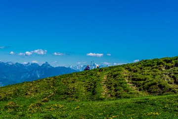 Zwei Personen sitzen auf einer Wiese in den Bergen und blicken auf das Alpen Panorama Allgäu Bayern 