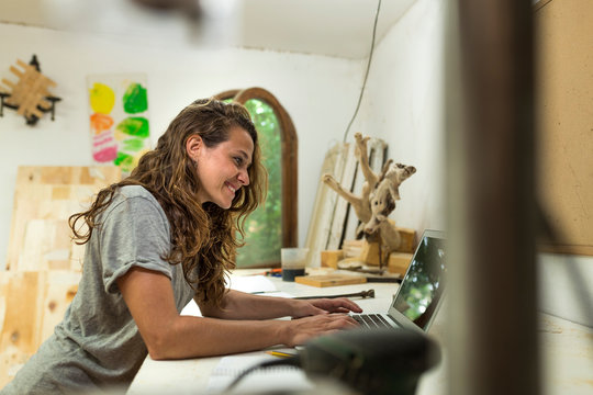 Side view of craftswoman using laptop at her desk