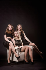 Obraz na płótnie Canvas Three beautiful girls in black evening dresses are sitting in the chair