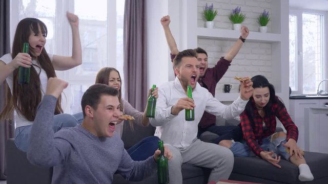 emotion, fans watching football match on TV with excitement and then rejoice at the victory sitting on the couch with a beverages and pizza at home