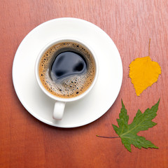 White cup with black coffee and autumn leaves