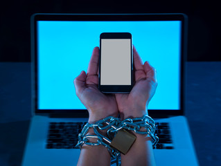 Man hands tied to mobile phone with chain padlock in internet or social media addiction