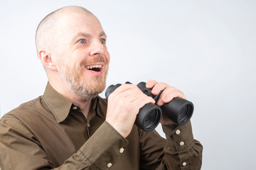 Bearded man with binoculars in his hands looking with joy and surprise in the distance on a white background