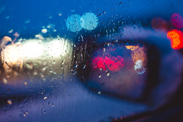 Night city road through windshield cars abstract background water drop on the glass lights and rain