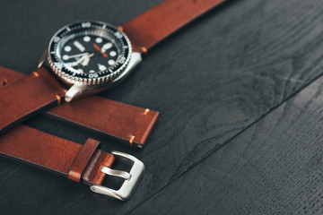 Mens diver watch with brown leather handmade watch strap on black wooden surface. Closeup. Copy space. 