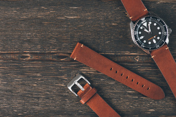Brown leather handmade watch strap on mens luxury watch laying on dark rustic wooden table. Close...