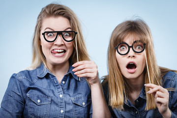 Two happy women holding fake eyeglasses on stick