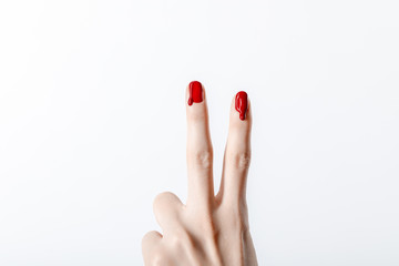 cropped view of woman showing peace sign with dripping red nail polish isolated on grey