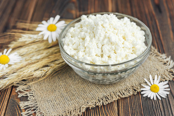 Cottage cheese with ears and chamomile on wooden background.