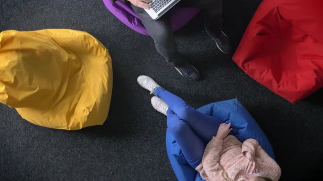 Circling Around Topshot Of Man Working With Laptop And Woman Talking On Cellphone Sitting On Multicoloured Bags.