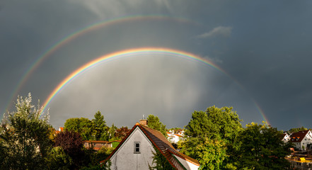 full double rainbow over dramatically lit houses