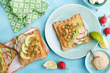 Toasts with chickpea hummus, avocado, fresh radish, cucumber, sesame seeds and flaxseed sprouts. Diet breakfast. Delicious and healthy plant-based vegetarian, vegan food. Flat lay. Top view