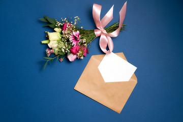 Wedding Marriage or Valentines Day composition: bunch of flowers kraft paper envelope with blank white letter with copy space lay on blue background. Mother's day banner for website, festive template