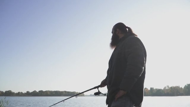 Man with beard is fishing on the river bank. Fisherman fishing with a fishing rod on the river. River fishing. Slow motion.