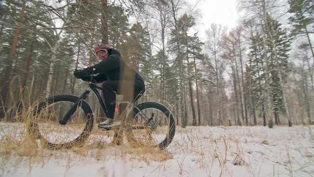 Professional extreme sportsman biker sit a fat bike in outdoors. Cyclist recline in the winter snow forest. Man walk with mountain bicycle with big tire in helmet and glasses. Slow motion in 60fps.