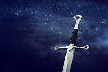 low key image of silver sword. fantasy medieval period. Glitter overlay.