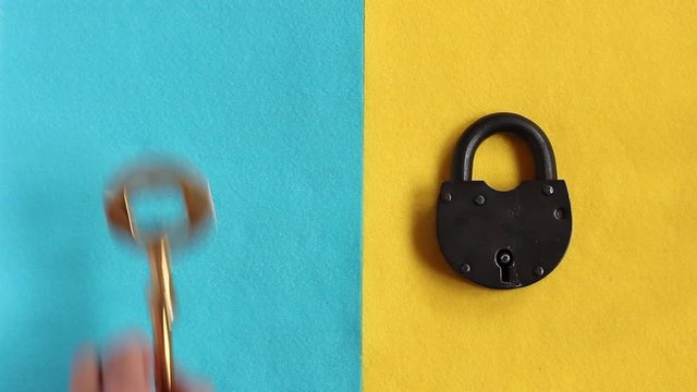 male hand puts the black padlock on yellow felt, then puts three vintage golden keys on blue felt and opens padlock, close-up 