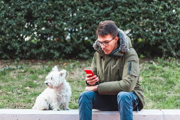 Young man sitting in the park with his dog using smartphone