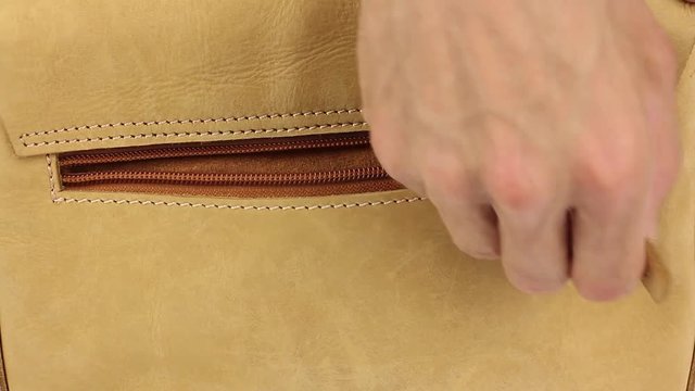 human hand opens hidden zippered pocket on bag made from natural yellow leather, then puts his hand in pocket, takes his hand out, then close pocket