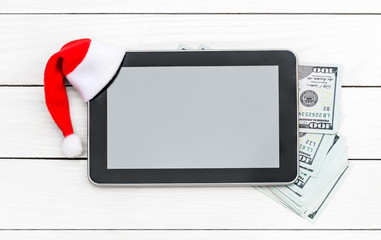 Santa's hat on tablet PC and money on wooden background. Top view. Space for text.