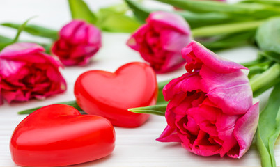 Tulips with two red hearts on white wooden background.