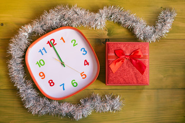 Image of decorated clock showing midnight and gift in beautiful red box on wooden table.