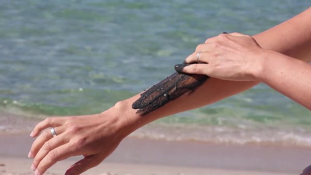 the girl gently covers her hand and the palm with therapeutic mud, on the background of sea beach 