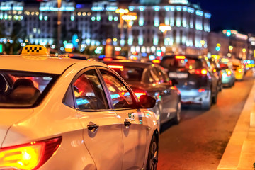 taxi in traffic jam among street cars in the evening rush hour in megalopolis on background of lights of the night city and bokeh
