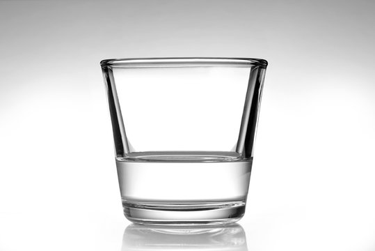 Bicchiere di acqua mezzo vuoto su un fondo da bianco a grigio