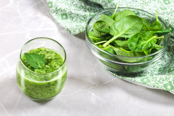 Green healthy smoothie in a cup decorated with a spinach leaf and a bowl of fresh spinach in the...