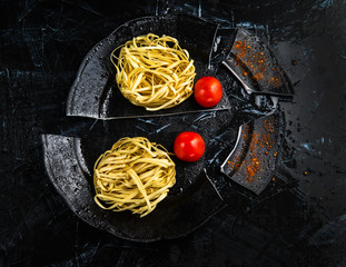 Uncooked Italian Fettuccine Pasta on a Broken Black Plate with Cherry Tomatoes