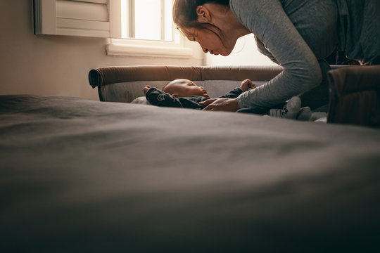 Mother Putting Her Baby In A Bedside Baby Crib