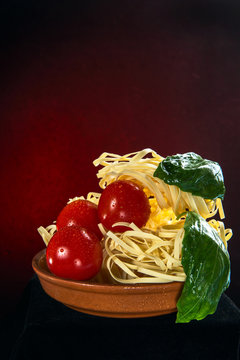 Uncooked Italian Fettuccine pasta in a ceramic plate. Decorated with basil and cherry tomatoes