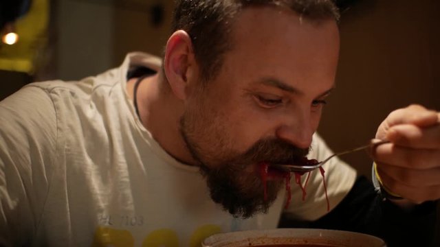 man with a beard eating borsch with sour cream. red-beet soup. borsh