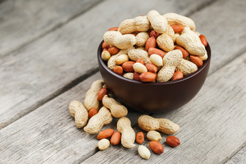 Roasted peanuts in the shell and peeled in a cup, against a gray wooden table