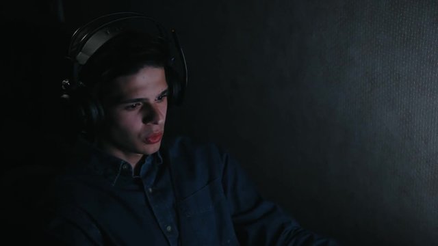 positive man listening music and sing along in headphones on computer at night
