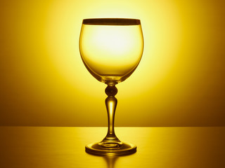 Transparent wine glass with a thin leg on a golden background with a gradient
