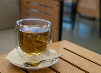 A cup of tea with saucer and spoon on wooden table.