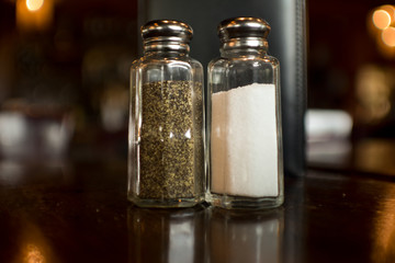 close up of salt and pepper shaker against black menu on a reflective table in a dark moody restaurant