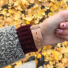 Golden women's wrist watches on the hand against the background of autumn foliage
