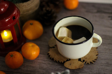 Coffee with marshmallow in a white cup on a blurred wooden background. In frame view a red lantern, mandarins. Holiday concept