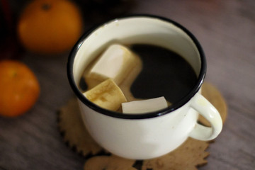 Coffee with marshmallow in a white cup on a blurred wooden background. In frame view a red lantern, mandarins. Holiday concept