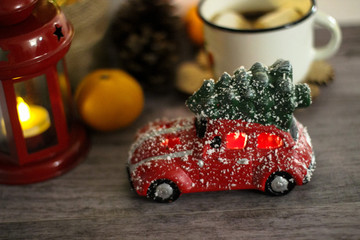 Red toy car with Christmas tree in the roof.  In a blurred background white cup, red lantern, mandarins. Holiday concept