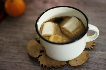 Coffee with marshmallow in a white cup on a blurred wooden background. In frame view a red lantern, mandarins. Holiday concept