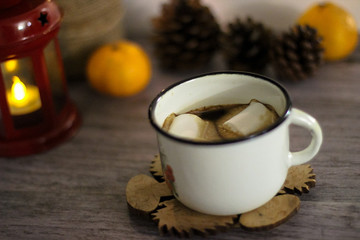 Coffee with marshmallow in a white cup on a blurred wooden background. In frame view a red lantern, mandarins. Holiday concept