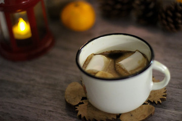 Coffee with marshmallow in a white cup on a blurred wooden background. In frame view a red lantern, mandarins. Holiday concept