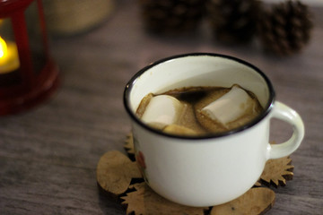 Coffee with marshmallow in a white cup on a blurred wooden background. In frame view a red lantern, mandarins. Holiday concept